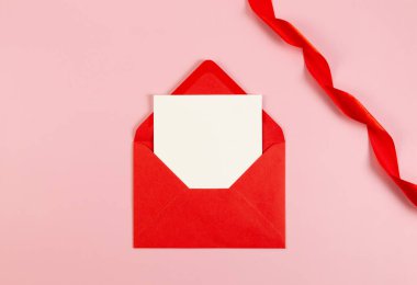 Kırmızı zarfın üst görüntüsü, beyaz kart ve pembe arka planda kırmızı kurdele. Sevgililer Günü, aşkım. Parlak rulo kumaş, ipek ve saten kumaş. Boşluğu kopyala, düzleştir, gönder.