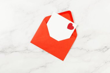 Kırmızı zarfın üst görüntüsü, beyaz mermer arka planda beyaz kart. Sevgililer günü, kırmızı kalp, aşk. Düz yatay, kopyala boşluk.