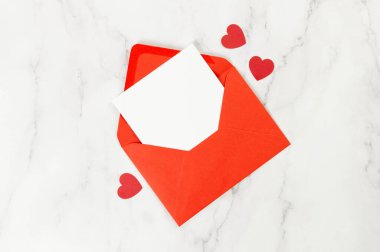 Kırmızı zarfın üst görüntüsü, beyaz mermer arka planda beyaz kart. Sevgililer günü, kırmızı kalpler, aşk. Düz yatay, kopyala boşluk.