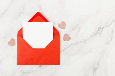 Kırmızı zarfın üst görüntüsü, beyaz mermer arka planda beyaz kart. Sevgililer günü, pembe parıltılı kalpler, aşkım. Düz yatay, kopyala boşluk.