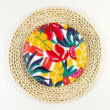 Kahverengi hasır masa paspasının üst görüntüsü, beyaz arka planda renkli plaka. Saman tepsisi, egzotik bitki tabağı, yaz pikniği. Düz yat, boşluğu kopyala. 