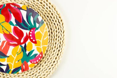 Kahverengi hasır masa paspasının üst görüntüsü, beyaz arka planda renkli plaka. Saman tepsisi, egzotik bitki tabağı, yaz pikniği. Düz yat, boşluğu kopyala. 