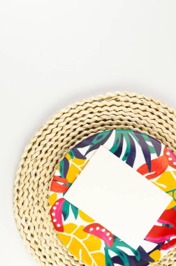 Kahverengi hasır masa paspası, beyaz kart, beyaz arka planda renkli plaka. Saman tepsisi, egzotik bitki tabağı, yaz pikniği. Düz yat, boşluğu kopyala. 