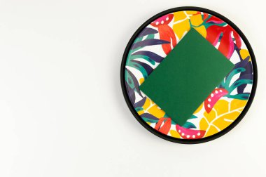 Siyah tepsinin üst görüntüsü, renkli plaka, beyaz arka planda yeşil kart. Egzotik bitki plakası, yaz pikniği. Düz yat, boşluğu kopyala.