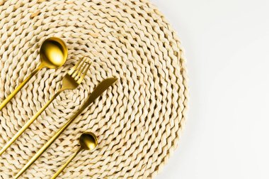 Kahverengi hasır masa paspası, beyaz arka planda altın çatal bıçak takımı. Saman yuvarlak tepsi, düz konum, kopyalama alanı. 