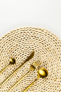 Kahverengi hasır masa paspası, beyaz arka planda altın çatal bıçak takımı. Saman yuvarlak tepsi, düz konum, kopyalama alanı. 