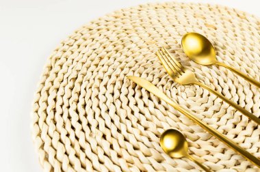 Kahverengi hasır masa paspası, beyaz arka planda altın çatal bıçak takımı. Saman yuvarlak tepsi, düz konum, kopyalama alanı. 