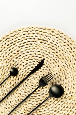 Kahverengi hasır masa paspası, beyaz arka planda siyah çatal bıçak takımı. Saman yuvarlak tepsi, düz konum, kopyalama alanı. 