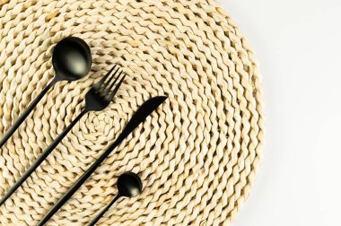 Kahverengi hasır masa paspası, beyaz arka planda siyah çatal bıçak takımı. Saman yuvarlak tepsi, düz konum, kopyalama alanı. 