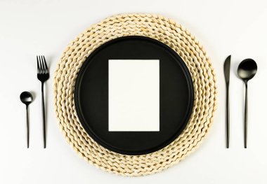 Kahverengi hasır masa paspası, siyah tabak, beyaz arka planda siyah çatal bıçak. Beyaz kart, saman yuvarlak tepsi, düz konum, kopyalama alanı. 