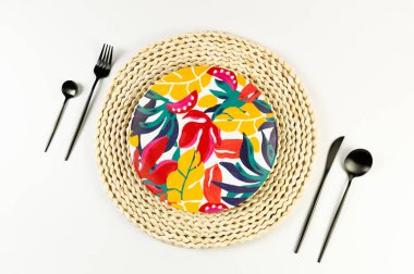 Kahverengi hasır masa paspası, renkli tabak, beyaz arka planda siyah çatal bıçak. Saman tepsisi, egzotik bitki tabağı, yaz pikniği. Düz yat, boşluğu kopyala. 