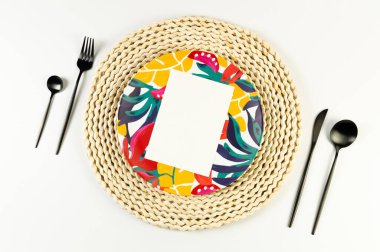 Kahverengi hasır masa paspası, renkli tabak, beyaz arka planda siyah çatal bıçak. Beyaz kart, saman yuvarlak tepsi, egzotik bitki tabağı, yaz pikniği. Düz yat, boşluğu kopyala. 