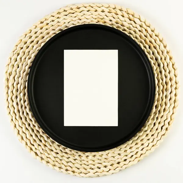 Kahverengi hasır masa paspası, siyah plaka, beyaz arka planda beyaz kart. Saman yuvarlak tepsi, düz konum, kopyalama alanı. 