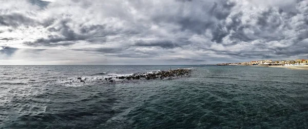 都市のスカイラインと荒い海を持つOstia Lidoのローマ海岸の上の悪天候と劇的な空のパノラマビュー一方 ネプチューン像の上にカラスが眠っています — ストック写真