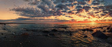 Golden sun dips below horizon, casting a warm glow over the ocean, waves crashing and sky transforms into a canvas of orange, pink and purple hues, mammatus clouds add texture and drama.