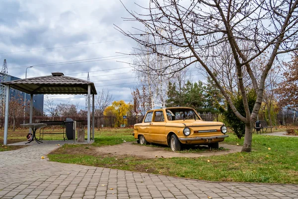 Photography on theme super old retro car Zaporozhets stands in park with flat tires, photo consisting of very old retro car with broken glass after an accident to park, old retro car at park no people