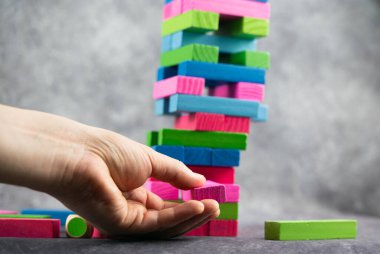 Canlı bir el renkli Jenga kulesiyle ustaca etkileşime giriyor, dikkat çekici bir hassasiyet ve denge sergiliyor.