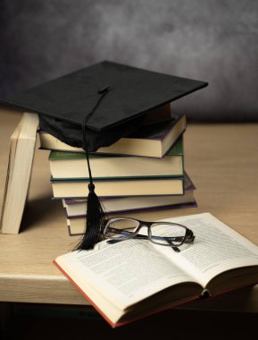 Eğitimdeki başarıyı simgeleyen istiflenmiş kitapların mezuniyet şapkası. Gözlükler bilimsel bir dokunuş ekler..