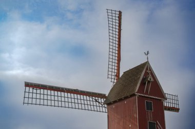 Canlı kırmızı bir yel değirmeni bulutlu bir gökyüzünün altında, zamansız ve klasik mimarisini gözler önüne seriyor.