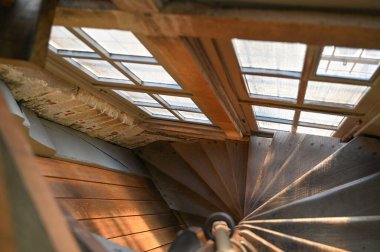 Güneş ışığıyla aydınlatılan sarmal merdivenlerin büyüleyici görüntüsü, zengin ahşap dokuları ve zarif tasarımı vurguluyor.