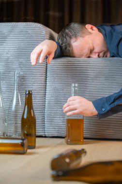 Bir adam boş şişelerin arasında kanepede dinleniyor. Alkol mücadelesinin etkilerini ve sonuçlarını yansıtıyor.