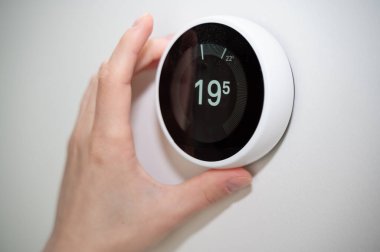 Bir el, modern akıllı termostatı en uygun konfor ve enerji verimliliğini elde etmek için ustalıkla ayarlar.