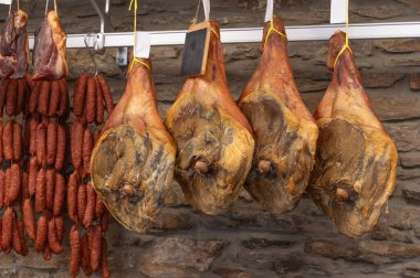 Etlerin çeşitli çeşitleri zarif bir şekilde sergileniyor, sağlam bir askıda asılı, farklı türde sosislerle birlikte lezzetli jambonlar da var.