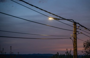 Arka planda muhteşem bir günbatımı olan uzun bir direğe asılmış bir sokak lambası büyüleyici bir akşam sahnesi yaratıyor.