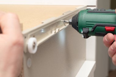 Yakın plan çekimde, kablosuz matkap kullanarak bir donanımı, işçiliği ve hassasiyeti güvenle tutturan bir el görülüyor.