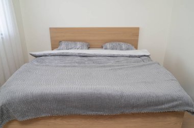 Huzurlu ve minimalist bir yatak odası tasarımı. Doğal ahşap bir çerçeve ile tamamlanmış yumuşak gri bir yatak odası.