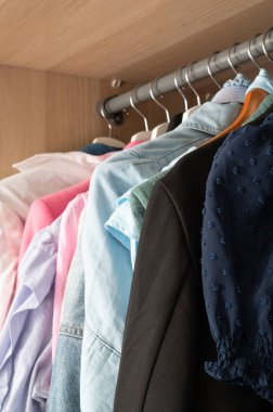 Canlı bir kıyafet çeşidi düzgün bir şekilde düzenlenmiş ve bir gardıroba asılmış, farklı stiller sergileniyor.