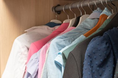 Kıyafetlerle dolu bir dolap. Diğer giysi ve aksesuarlar arasında pembe bir gömlek de var.