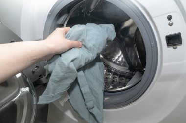 Bir kişi şu anda çamaşır makinesine havlu yerleştiriyor. Çamaşır makinesini temizlemek için çok önemli bir cihaz.