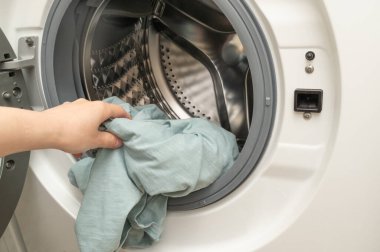 Bir birey, giysilerini iyice temizlemek amacıyla çamaşır makinesine dikkatlice yerleştiriyor.