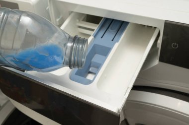 Işıl ışıl mavi sıvıyla dolu bir şişe kullanım için belirlenmiş bir çamaşır makinesinin kompartımanına dökülüyor.