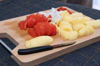 Canlı kırmızı domatesler ve ahşap kesim tahtasının üzerinde güzel dilimlenmiş topraksı patatesler, yemek hazırlığı için ideal.