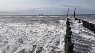 Dinamik okyanus dalgaları sürekli kıyıya vurur ve ahşap yapıların yer aldığı sakin bir sahil manzarası yaratır.