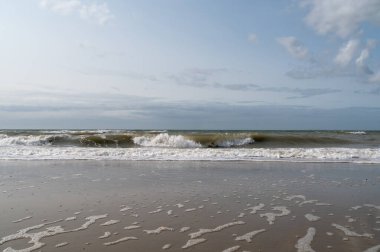 Güzel ve canlı bir gökyüzünün altında kumlu bir plaja yuvarlanan yumuşak dalgaların sakin ve sakin bir sahnesi.