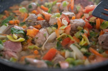 Sıcak tavada kızartılmış taze, gevrek sebzeler ve taze et parçalarının canlı ve renkli bir karışımı.