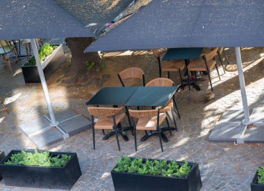 Güneşden ve gölgeden korunmak için büyük şemsiyelerin altında konforlu masa ve sandalyelerin olduğu güzel bir teras alanı.