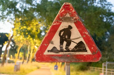 Kazı yapan bir adamın görüntüsünün yer aldığı koyu kırmızı ve beyaz bir tabela, yoldan geçenlere önemli bilgiler iletiyor.