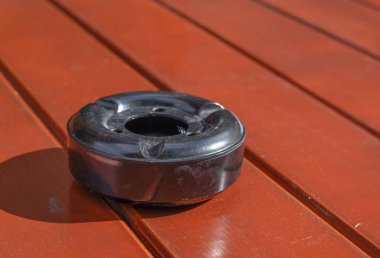 Parlak siyah bir kül tablası, ahşap ahşabın zarafetini ve zengin ahşap kaplamasını gösteren güzel bir ahşap masanın üzerinde belirgin bir şekilde sergilenir.