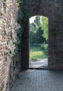 Zarif bir kemer açılışı, antik tuğla duvarlarla ustalıkla çerçevelenmiş huzurlu ve sakin yeşil bir manzarayı gözler önüne seriyor.