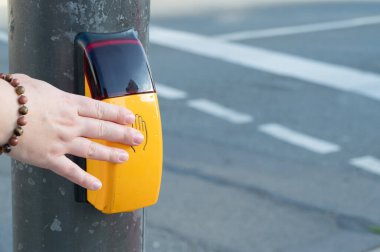 Bir el, trafiğe yakın bir yerde bulunan parlak sarı yaya geçidi düğmesiyle aktif olarak meşgul.