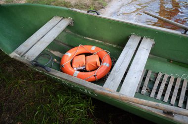 Parlak yeşil bir kano, içinde dinlenen bir can yeleği barındırıyor, su aktivitelerinde veya denizde acil durumlarda kullanılmaya hazır.
