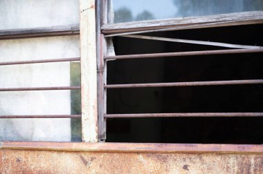 Bu, sağlam ahşap çerçeve içeren paslı bir pencerenin tasviri. Güvenliği artırmak için güçlü metal parmaklıklar ile tamamlanmış.