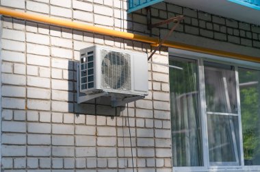 Sağlam tuğlalı bir binanın dış tarafına güvenli bir şekilde yerleştirilmiş bir havalandırma ünitesi, sıcak hava koşullarında gerekli soğutma hizmetlerini sağlıyor.