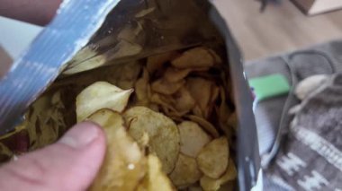 Bir el lezzetli patates cipsleriyle dolu bir torbaya uzanır ve eğlenceli atıştırmalık deneyimini ön plana çıkarır.