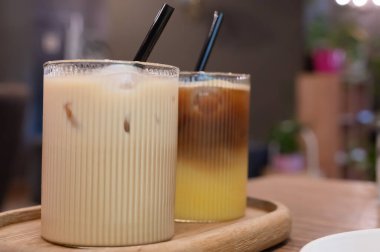 Ahşap tepside uzun bardaklarda servis edilen iki içecek. Kremalı içecek ve renkli bir içecek büyüleyici bir görsel tedavi sağlar..