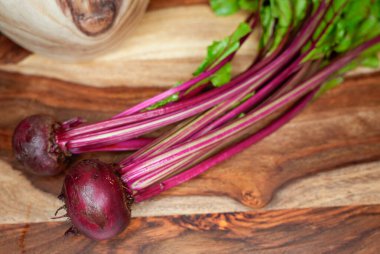 Canlı yeşil yaprakları olan taze organik pancarlar tahta kesme tahtasına yerleştirilmiş. Koyu kırmızı kökler ve uzun saplar kırsal ahşap zemin ile çok güzel tezat oluşturuyor..